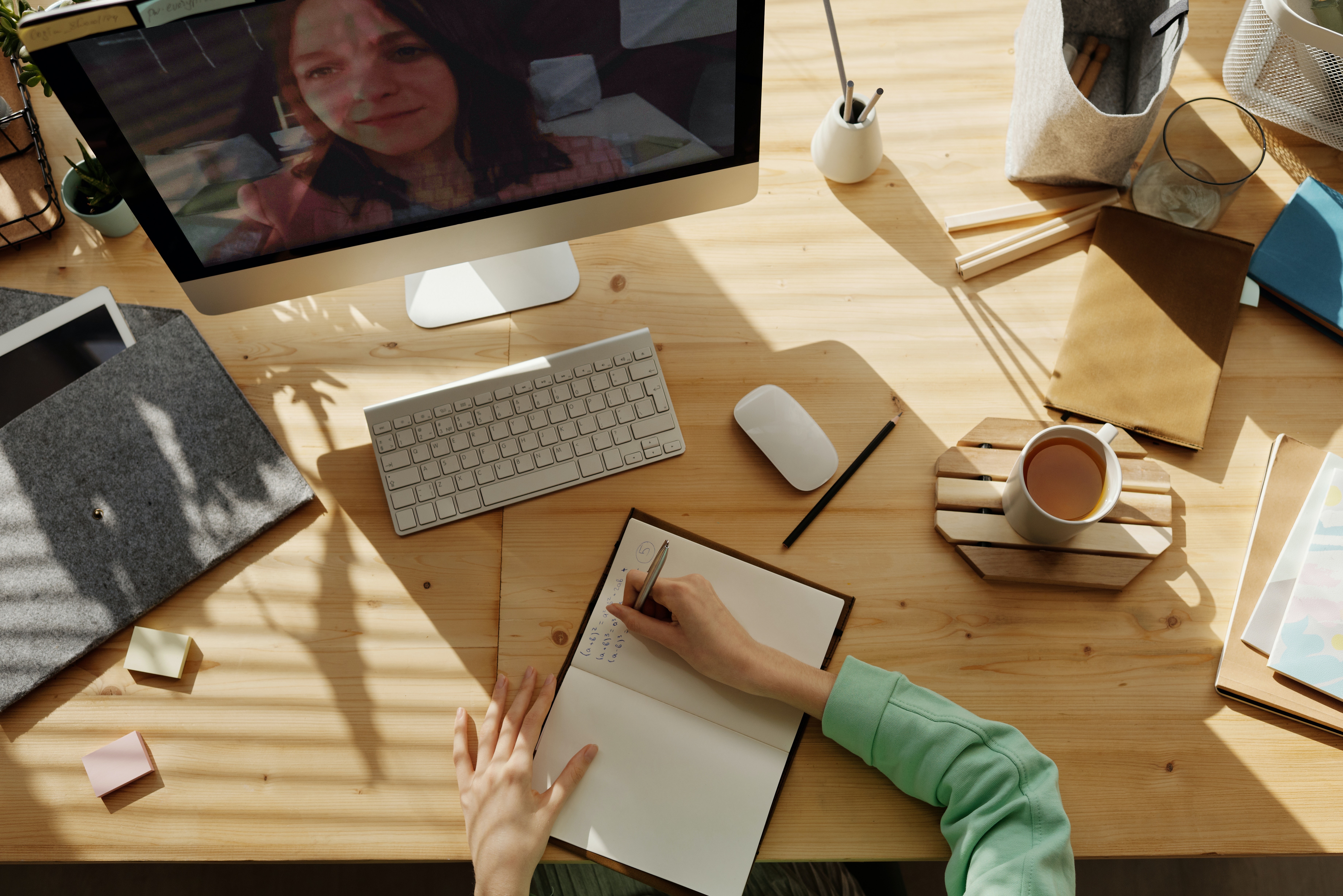 person sitting at table with coffee and computer writing on a notepad