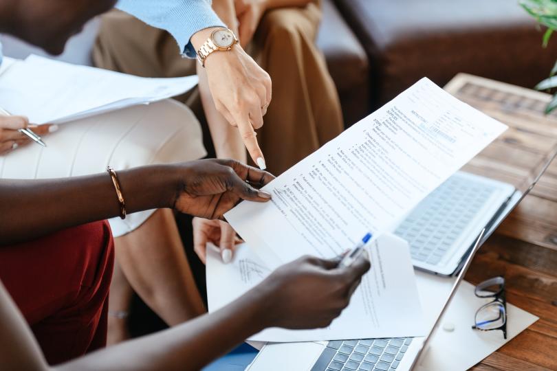 hands pointing to document above keyboard and eyeglasses resting on table